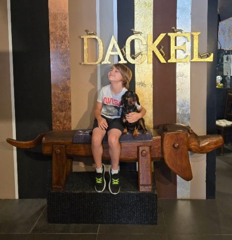 Junge sitzt auf einer riesigen Dackel-Skulptur im Dackelmuseum in Regensburg. Kurioses Ausflugsziel in Bayern für Familien und Tierliebhaber.