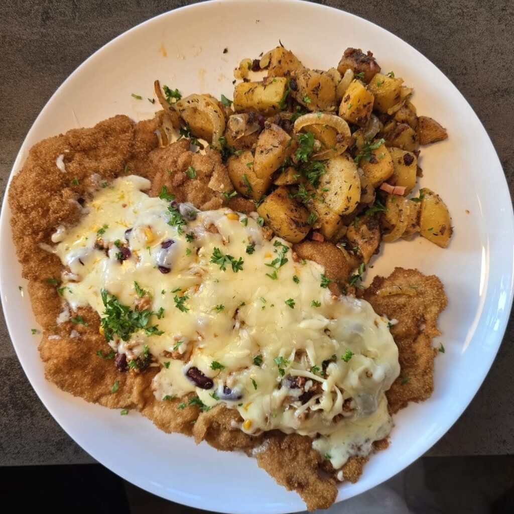Überbackenes XXL-Schnitzel mit geschmolzenem Käse, Zwiebeln und frischen Kräutern, dazu Bratkartoffeln – Spezialität im Schnitzelparadies Wendelstein, Ausflugsziel für Foodies in Bayern.