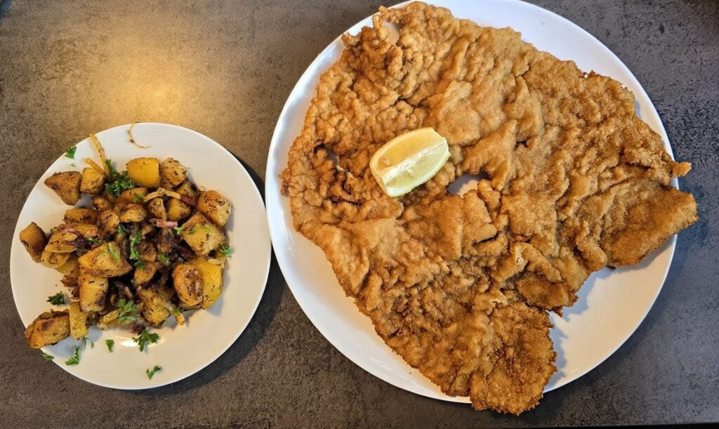 XXL-Schnitzel Wiener Art mit Zitrone und knusprigen Bratkartoffeln im Schnitzelparadies Wendelstein, beliebtes Restaurant in Bayern für riesige Portionen und deftige Küche.