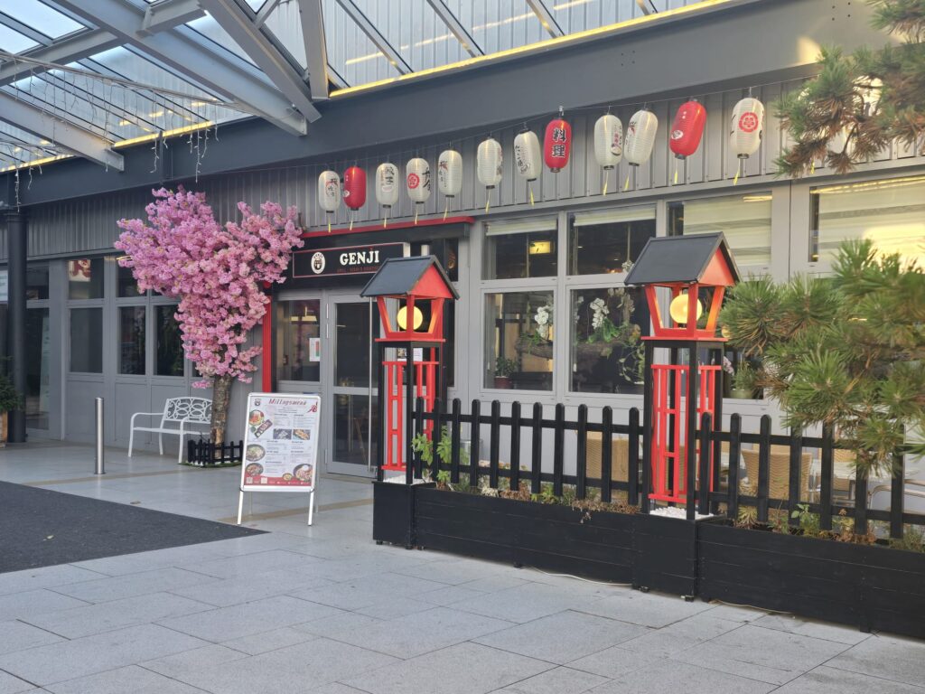 Eingang des Genji Asian Sushi & Grill in Neumarkt mit roten Laternen, Kirschblütenbaum und moderner Glasfassade