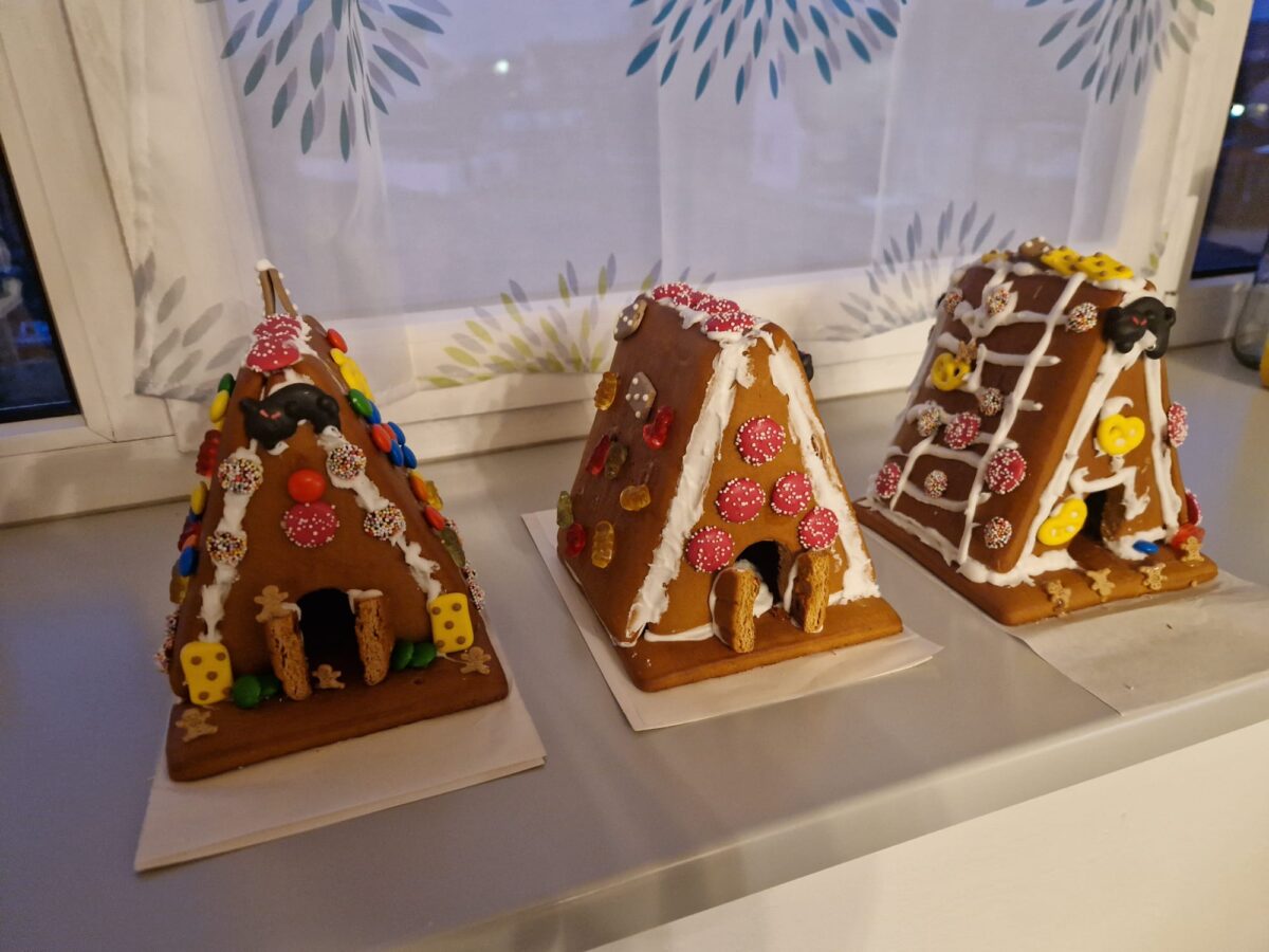 Drei selbst gebaute Lebkuchenhäuser mit bunter Deko aus Smarties, Gummibärchen und Zuckerguss stehen stolz auf der Fensterbank – leicht schief, aber mit ganz viel Herz gebaut.