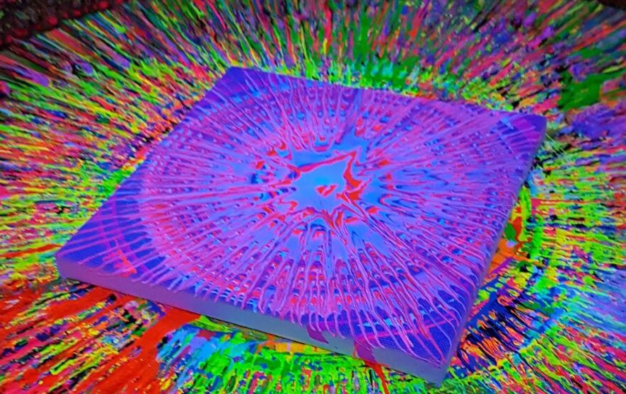 Buntes Spin-Art Kunstwerk aus Neonfarben auf einer drehenden Scheibe unter Schwarzlichtbeleuchtung.