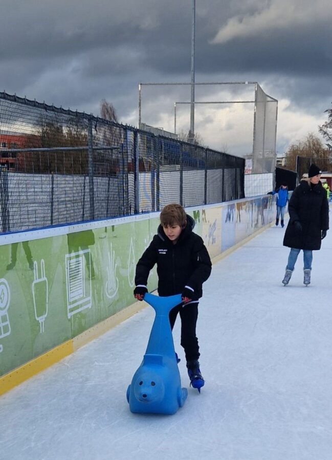 Kind fährt mit einem blauen Eislauf-Seehund über die Eisbahn in Neumarkt.